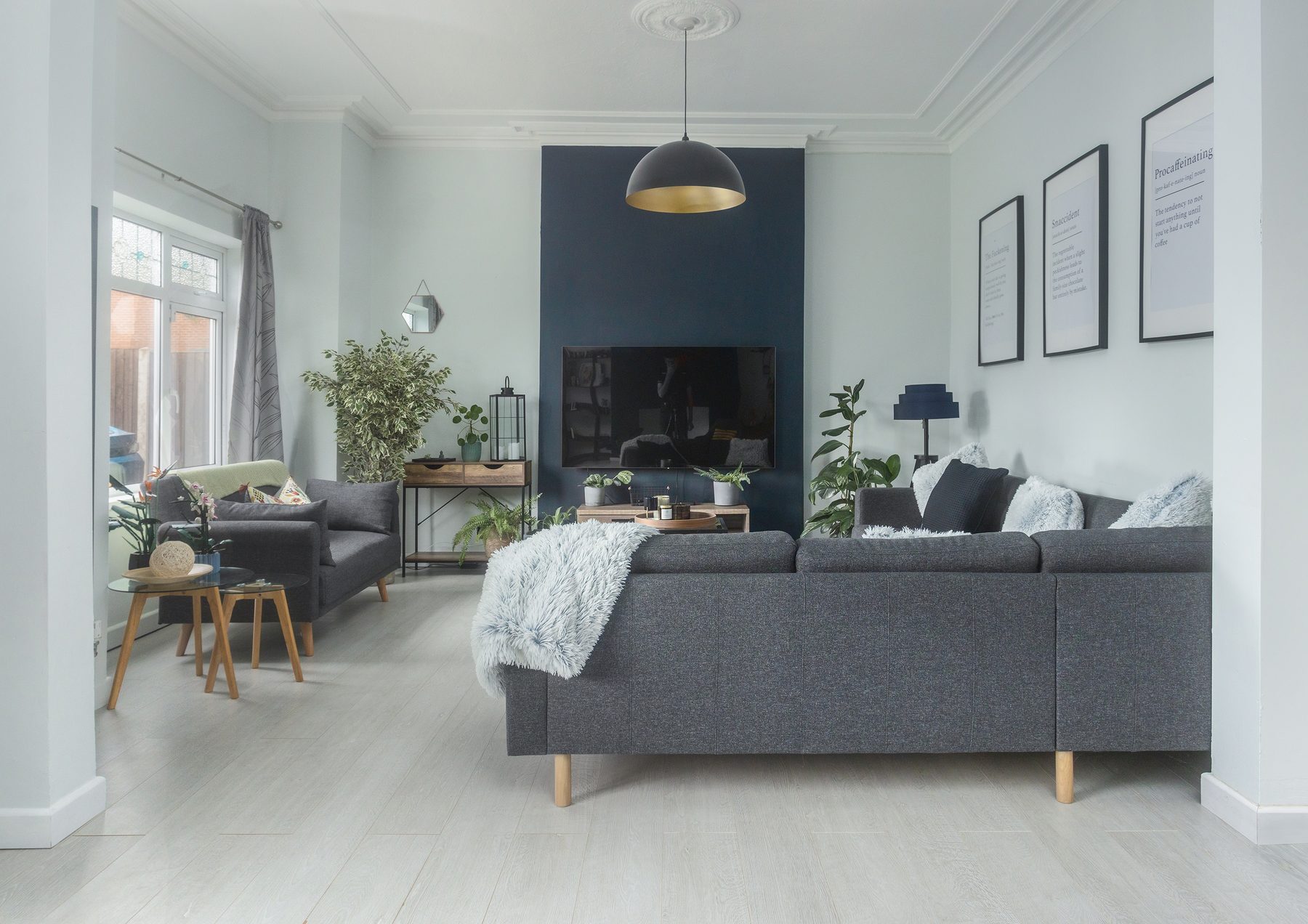 The bright Victorian living room at Willow Bank, with a deep grey corner sofa, houseplants and a large window.